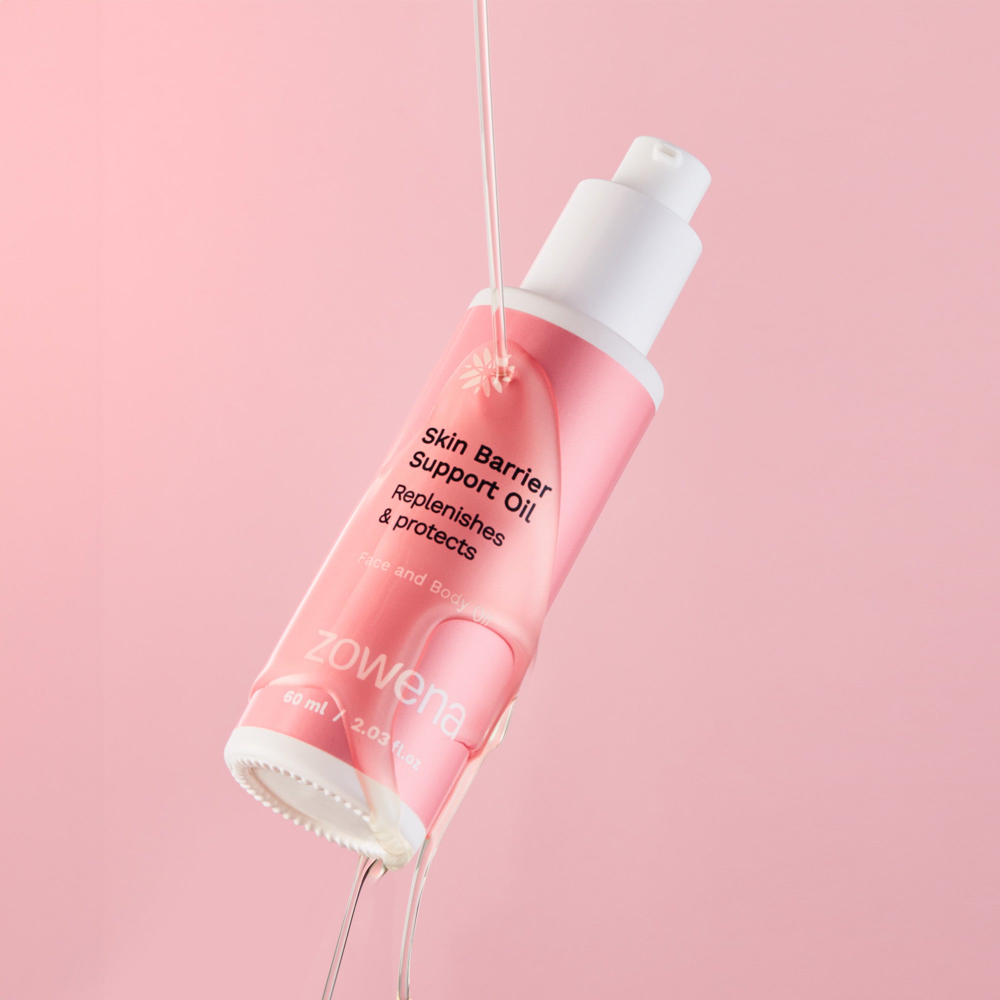 A bottle of Zowena Skin Barrier Support Oil suspended in mid-air against a soft pink background, with oil pouring from its dropper, showcasing its nourishing formula.