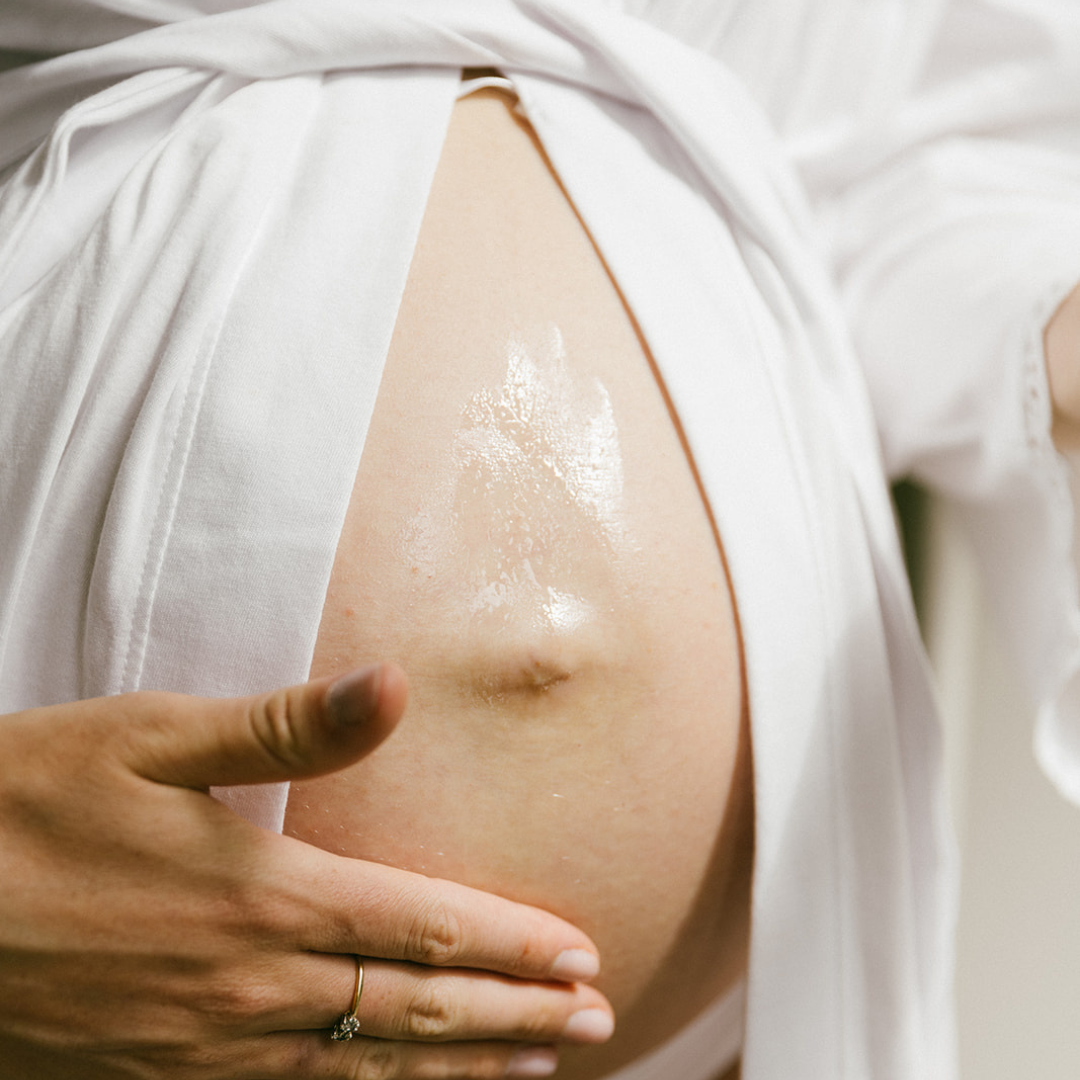 Pregnant belly with hand applying oil to moisturise